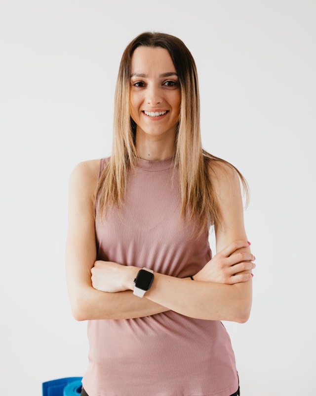 Nadia, smiling, arms crossed, in a pink tank top