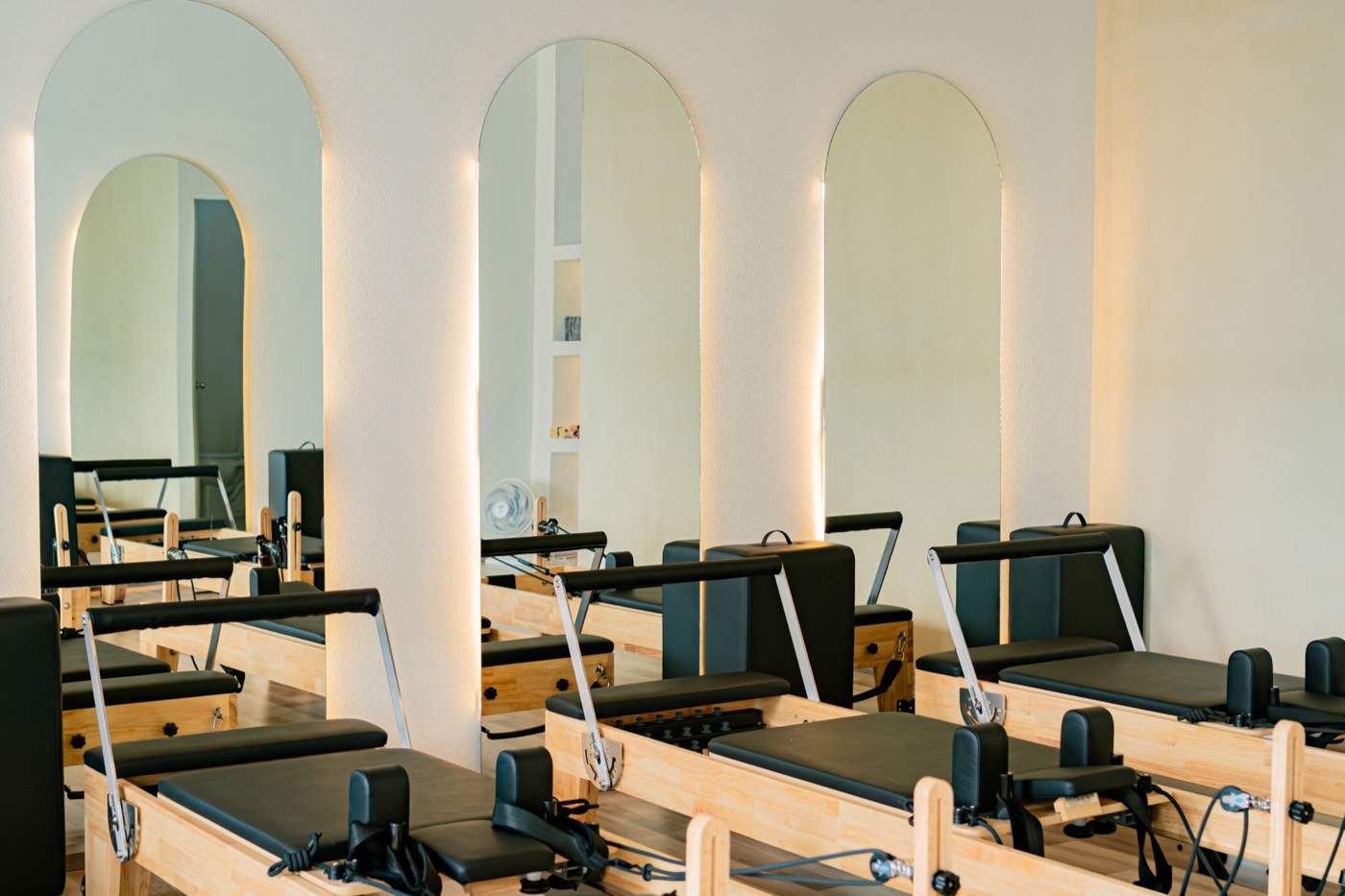 Wooden reformers lined up under backlit arched mirrors in a bright studio